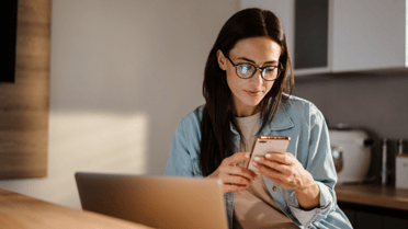 Woman sitting at laptop holding her phone