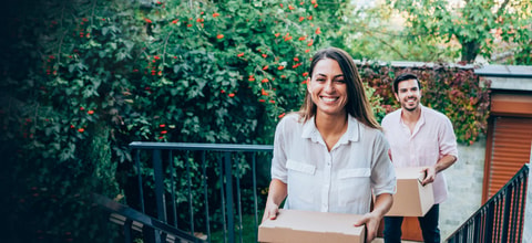 woman and man smile as they walk up steps moving in holding boxes