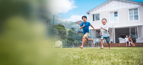2 parents watch by the backyard as 2 kids run on grass