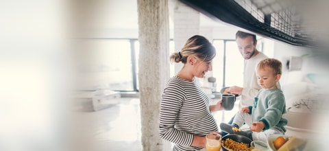 Pregnant woman and man smiling at their baby eating beans sitting on the kitchen counter