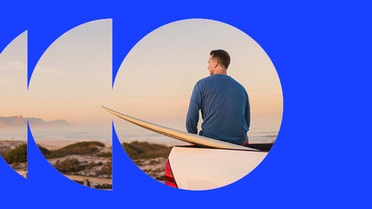 Person sitting on the back of a vehicle with a surfboard overlooking the coast.