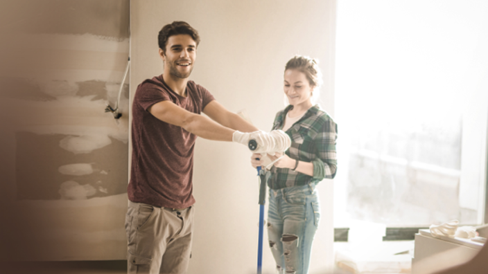 Couple smiling while holding paint brushes renovating